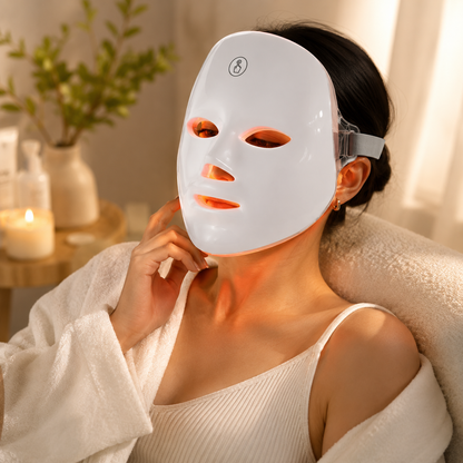 Person wearing a LED face mask in a cozy indoor setting with candles and plants.